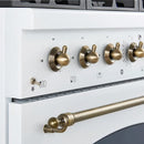 Close-up view of the control knobs on the Forno Antico 36-Inch Dual Fuel Range in white, featuring polished brass bezels, precise temperature markings, and a premium stainless steel panel.